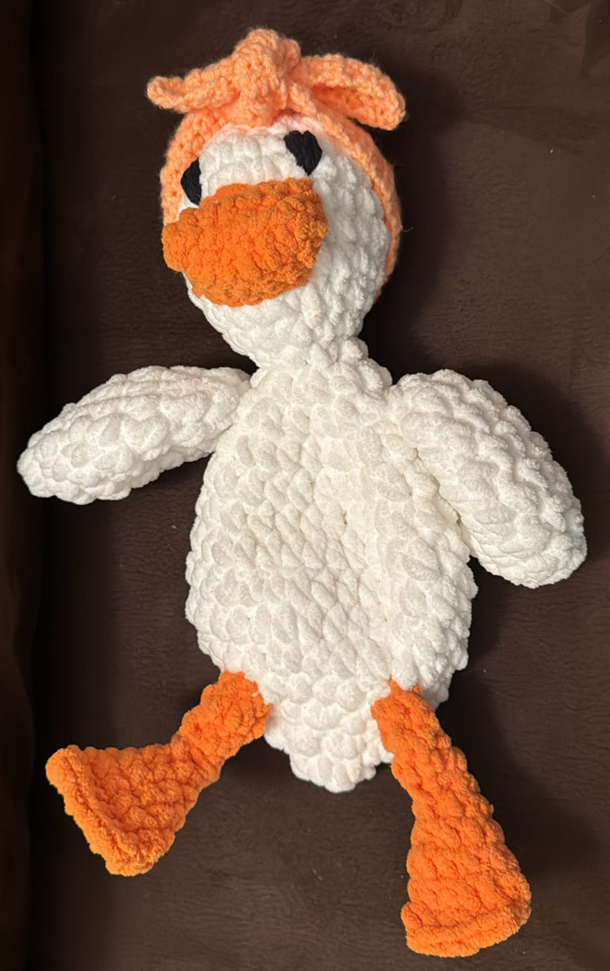 Crocheted toy duck with orange beak and feet on a brown background